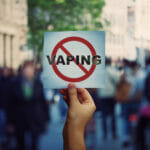 Human hand holding a protest banner stop vaping message over a crowded street background. Banning flavored vaping products to discourage people from smoking electronic cigarettes. Health risk concept.